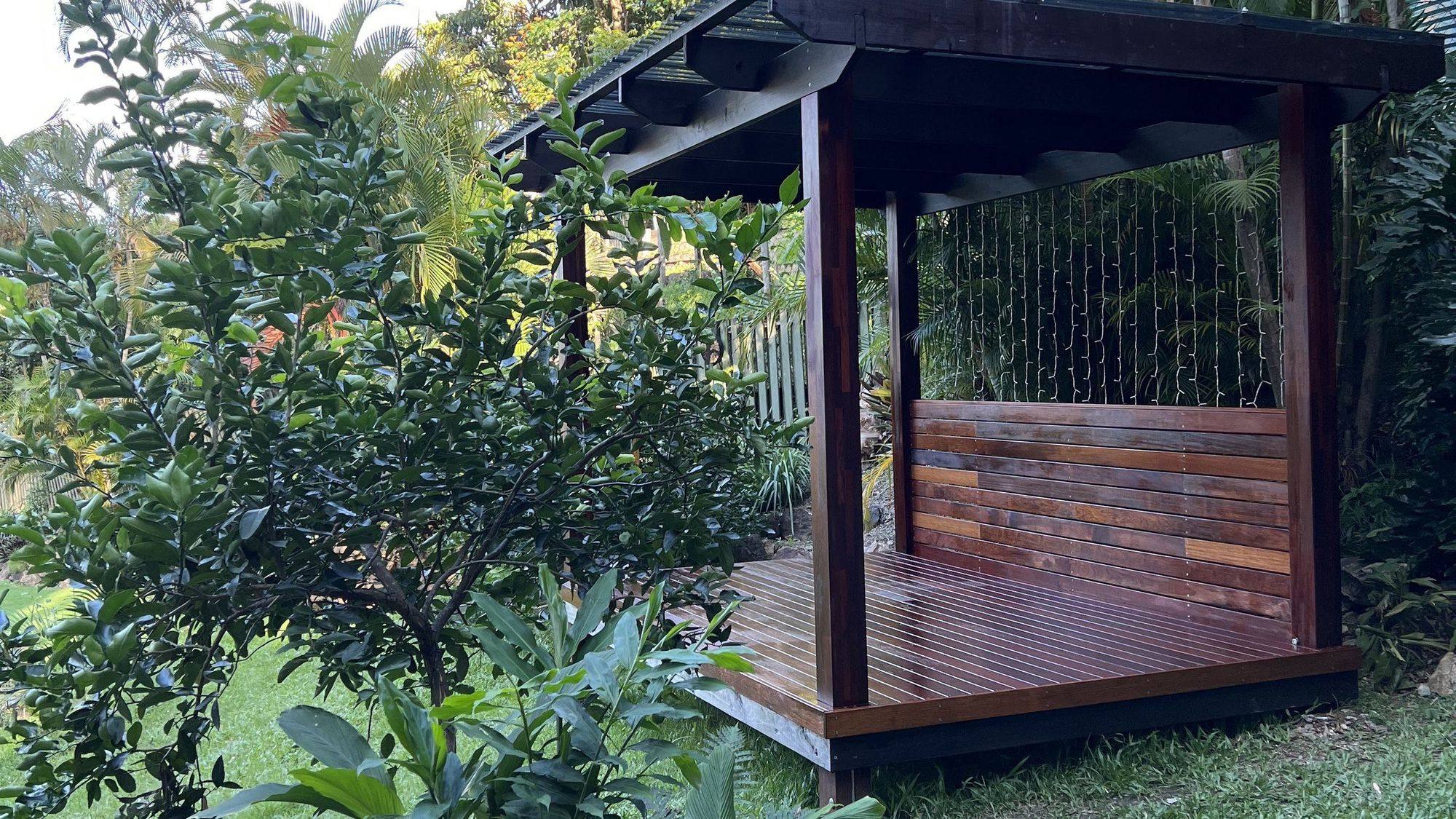 A hardwood gazebo standing on a lawn against dense subtropical planting