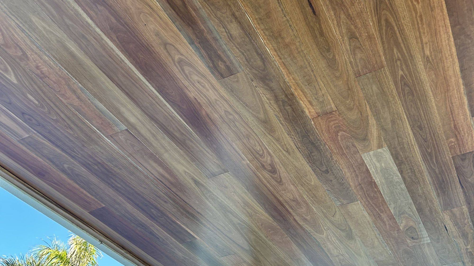 A hardwood-lined eave running out to a blue sky and palm fronds