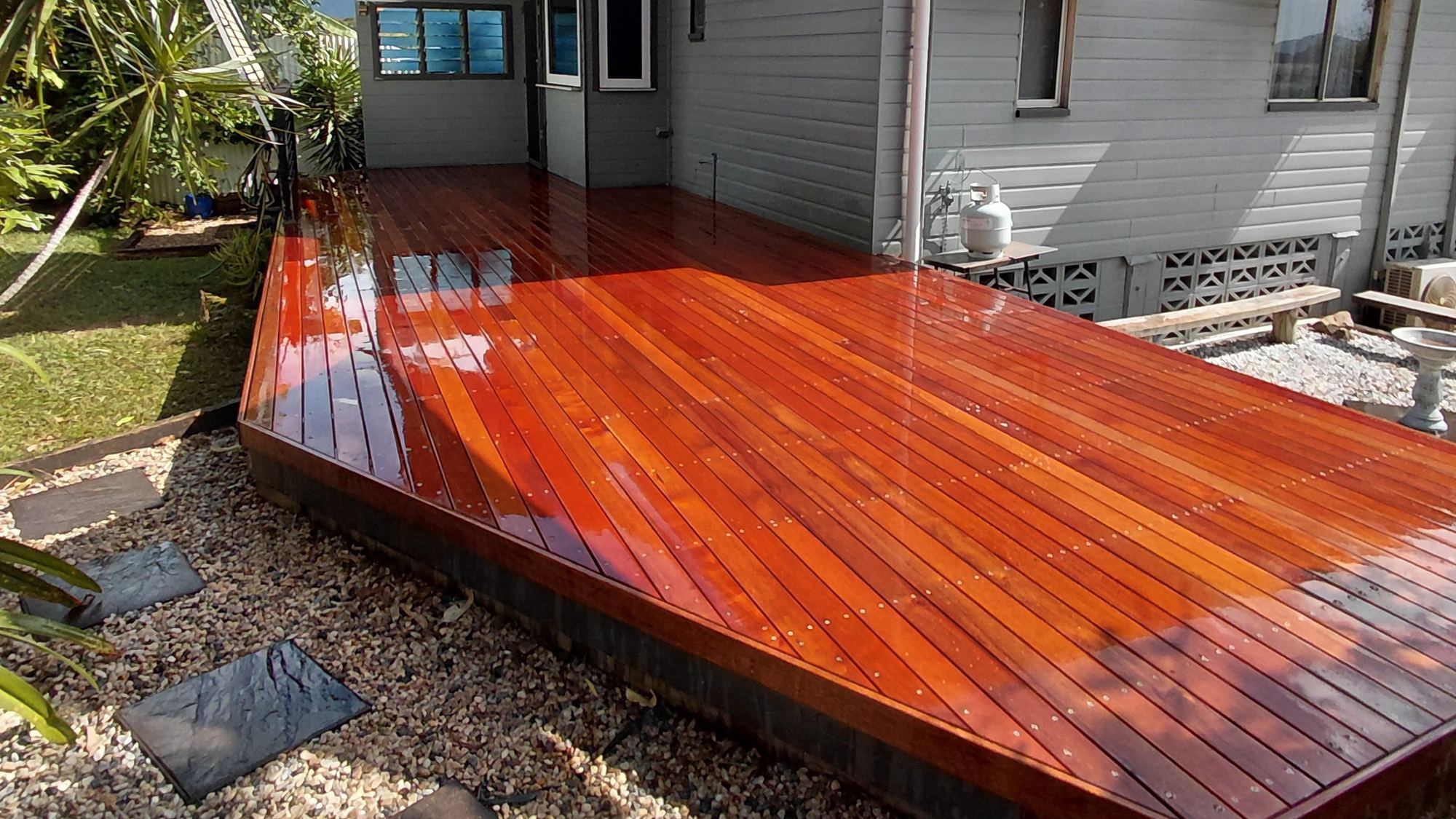A freshly oiled hardwood deck wrapping the side of a weatherboard home under a shade sail