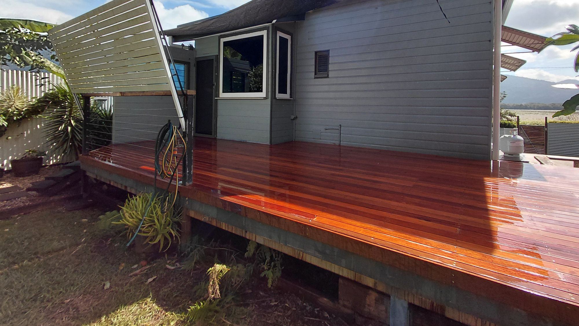 A wet, freshly oiled merbau deck wrapping around a weatherboard home with mountains behind