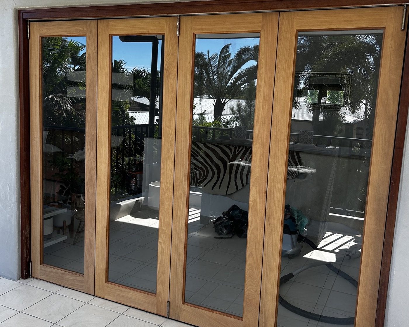 A set of timber-framed bifold doors opening from a tiled room onto a deck