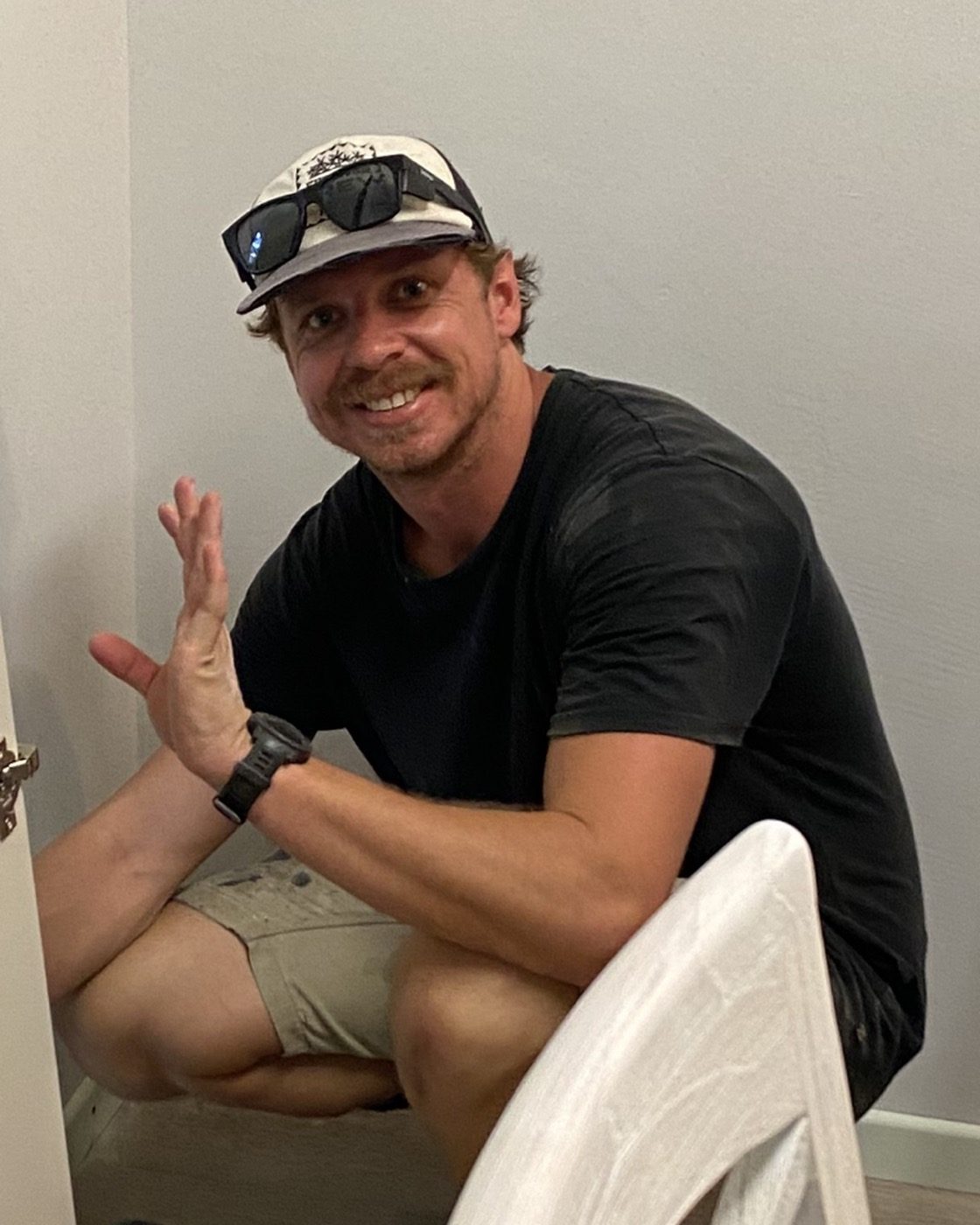 A carpenter crouched beside a freshly hung internal door with a sander on the floor beside him