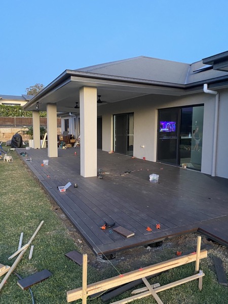 A large hardwood deck part-built at a modern home at dusk, with string lines and stakes set out