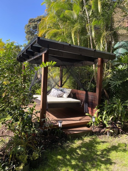 A hardwood pergola with a slatted screen and a hanging daybed in a palm garden