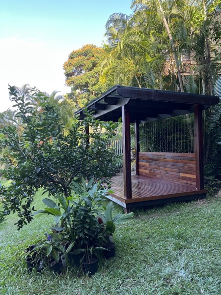 A hardwood gazebo standing on a lawn against dense subtropical planting