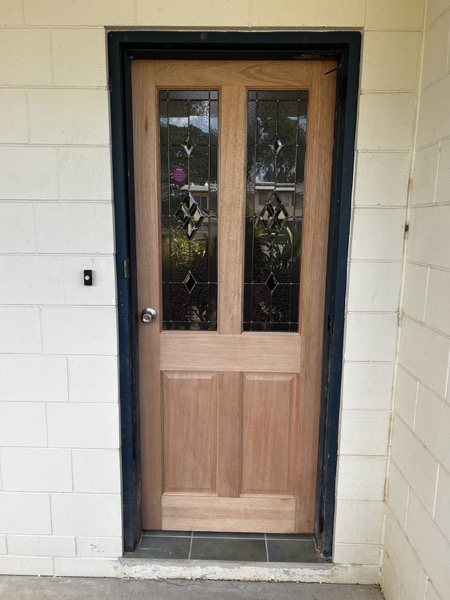 A timber front door with a glass panel set into a rendered wall