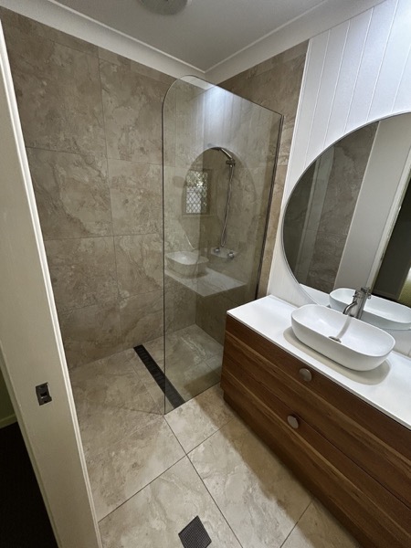 A renovated bathroom with a timber vanity, round mirror and glass shower screen
