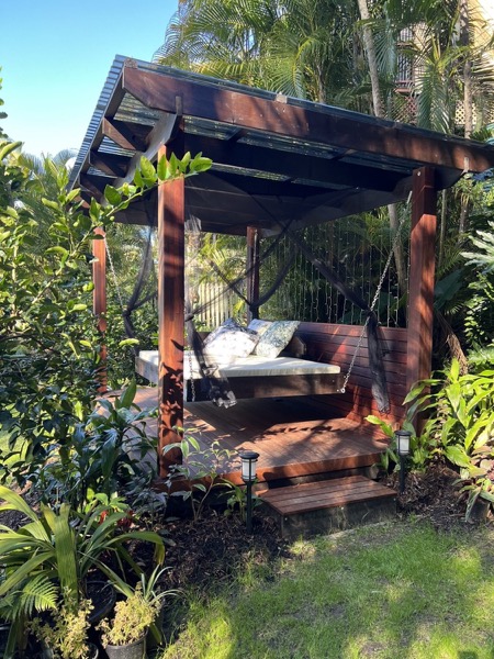 A hardwood pergola with a slatted screen and a daybed in a tropical garden